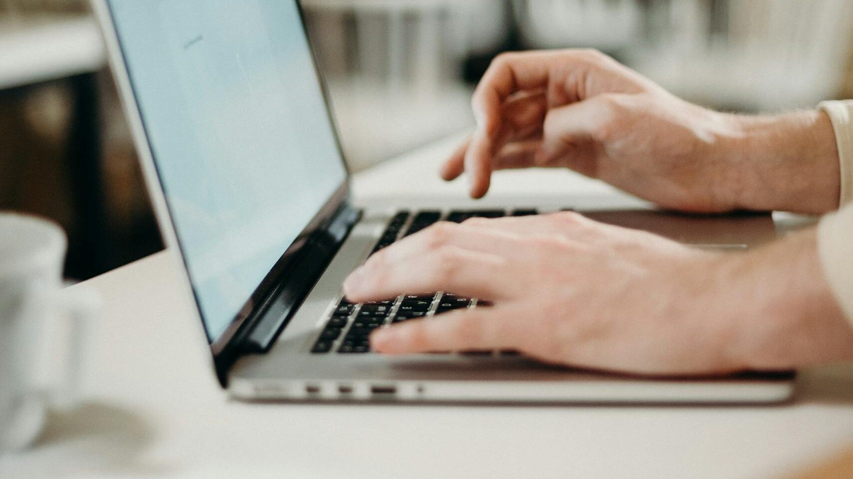 Close-up of hands typing on a laptop in a cozy indoor cafe setting.
